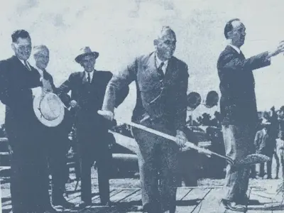 5 men on stage, man shoveling dirt at ground breaking ceremony